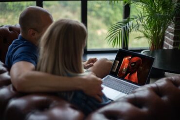 zwei Personen sitzen auf dem Sofa und schauen einen Film auf einem Laptop