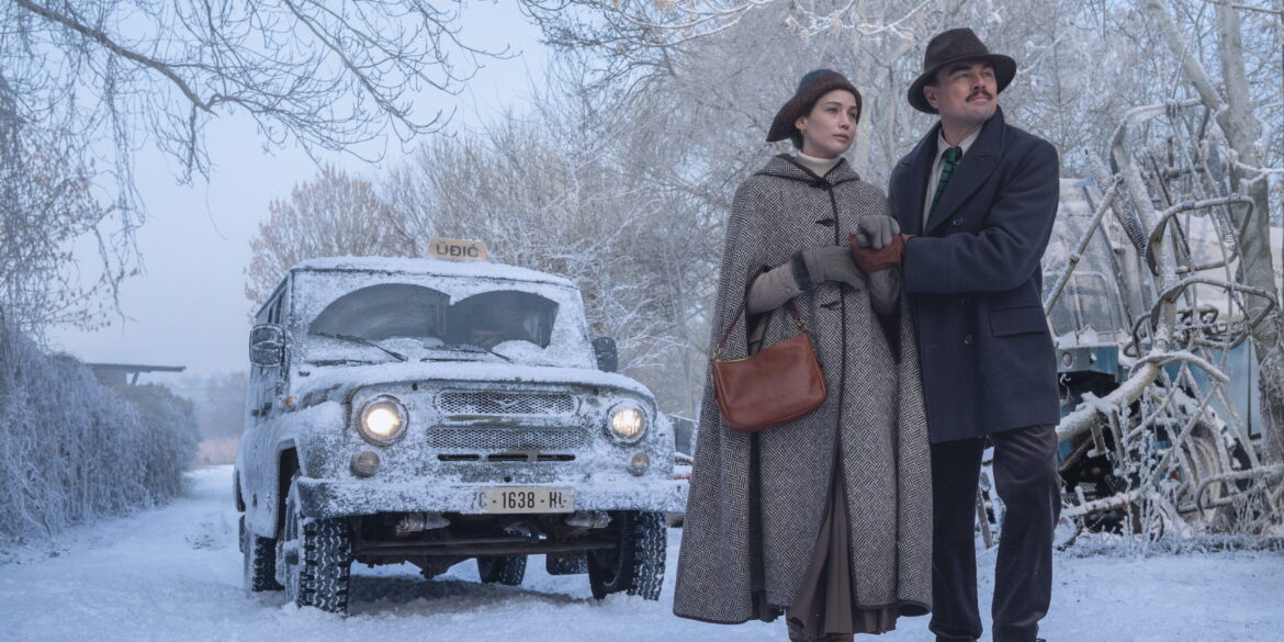 Eine Frau und ein Mann gehen über eine verschneite Straße. Hinter ihnen ist ein Auto zu sehen.