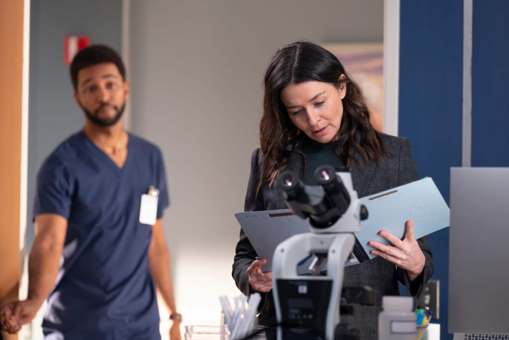 Ein Mann in blauer Arztkleidung steht in einem Büroraum, zusammen mit einer Frau, die gerade eine Akte anschaut