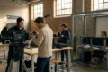 Fotorealistische Szene in einer deutschen Filmhochschule mit genau 4 Personen: eine Regiestudentin erklärt eine Szene vor einem Kamera-Setup, ein Kamerastudent justiert das Objektiv, eine Person sitzt am Schnittplatz im Hintergrund, eine weitere Person prüft den Ton, natürliches Licht durch hohe Fenster, realistische Texturen von Metall, Holz, Stoff und Kameraequipment. Moderne kreative Atmosphäre mit warmen neutralen Farben, klare Tiefenschärfe, glaubwürdige Hochschulumgebung ohne Schrift, Poster oder sichtbare Beschriftungen, kein Text.