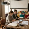Fotorealistische Szene in natürlichem Licht: ein moderner Besprechungsraum einer Filmproduktion in Deutschland mit genau 4 Personen an einem Holztisch, darauf ausgebreitete Drehbücher, Budgetpläne ohne sichtbare Schrift, ein Tablet, Storyboards ohne Text und ein kleines Modell einer Filmkamera. Im Hintergrund ein großes Fenster mit weichem Tageslicht, dezente Studioelemente, warme neutrale Farben, realistische Stoff-, Holz- und Metalltexturen, professionelle konzentrierte Stimmung, klare Komposition mit Fokus auf Zusammenarbeit, Finanzierung und Filmproduktion, keinerlei Text oder Schrift im Bild.