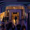 Fotorealistische Reisefotografie bei natürlichem Licht: eine einzelne Person steht auf einem historischen Platz zwischen markanten Filmkulissen, im Hintergrund eine europäische Altstadt und angedeutete Studioszenerie, dazu ein Reiseführer und ein Smartphone in der Hand, warme Abendsonne, realistische Steintexturen, glaubwürdige Kleidung, cineastische Tiefenschärfe. Die Szene soll Fernweh, Entdeckerfreude und Filmbezug ausstrahlen, mit natürlichen Farben, feinen Details in Architektur und Umgebung, ohne Text, ohne Schilder mit lesbaren Buchstaben, ohne Zahlen.