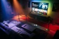 Fotorealistische Hero-Szene für einen Streaming-Vergleich: ein stilvolles Wohnzimmer bei Abendlicht, großer Fernseher mit unscharf angedeuteten Filmkacheln, vier unterschiedliche Stimmungswelten durch Licht und Farben symbolisiert, Sofa, Fernbedienung, Decke, dezente cineastische Atmosphäre, natürliche Beleuchtung, realistische Texturen, modernes hochwertiges Interior, kein Text im Bild