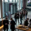 Photorealistic photograph of a modern cinema lobby with digital showtime screens, ticket booking kiosks, popcorn counter, and moviegoers comparing schedules on smartphones, natural lighting, realistic textures, contemporary multiplex atmosphere, no text in image