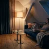 Fotorealistische Szene in einem gemütlichen deutschen Wohnzimmer am Abend: eine einzelne Person sitzt entspannt auf einem Sofa mit Fernbedienung in der Hand, auf dem großen Fernseher ist eine farbenfrohe Streaming-Oberfläche ohne lesbare Schrift zu sehen, daneben liegen Snacks und eine Decke, warmes natürliches Licht von einer Stehlampe trifft auf dezentes Blau aus dem Bildschirm. Realistische Texturen bei Stoffen, Holz und Glas, klare Tiefenschärfe, moderne aber wohnliche Einrichtung, stimmungsvolle Farben zwischen Dunkelblau, Orange und warmen Beigetönen, ein hochwertiger Editorial-Look ohne Text, Zahlen oder Logos im Bild.